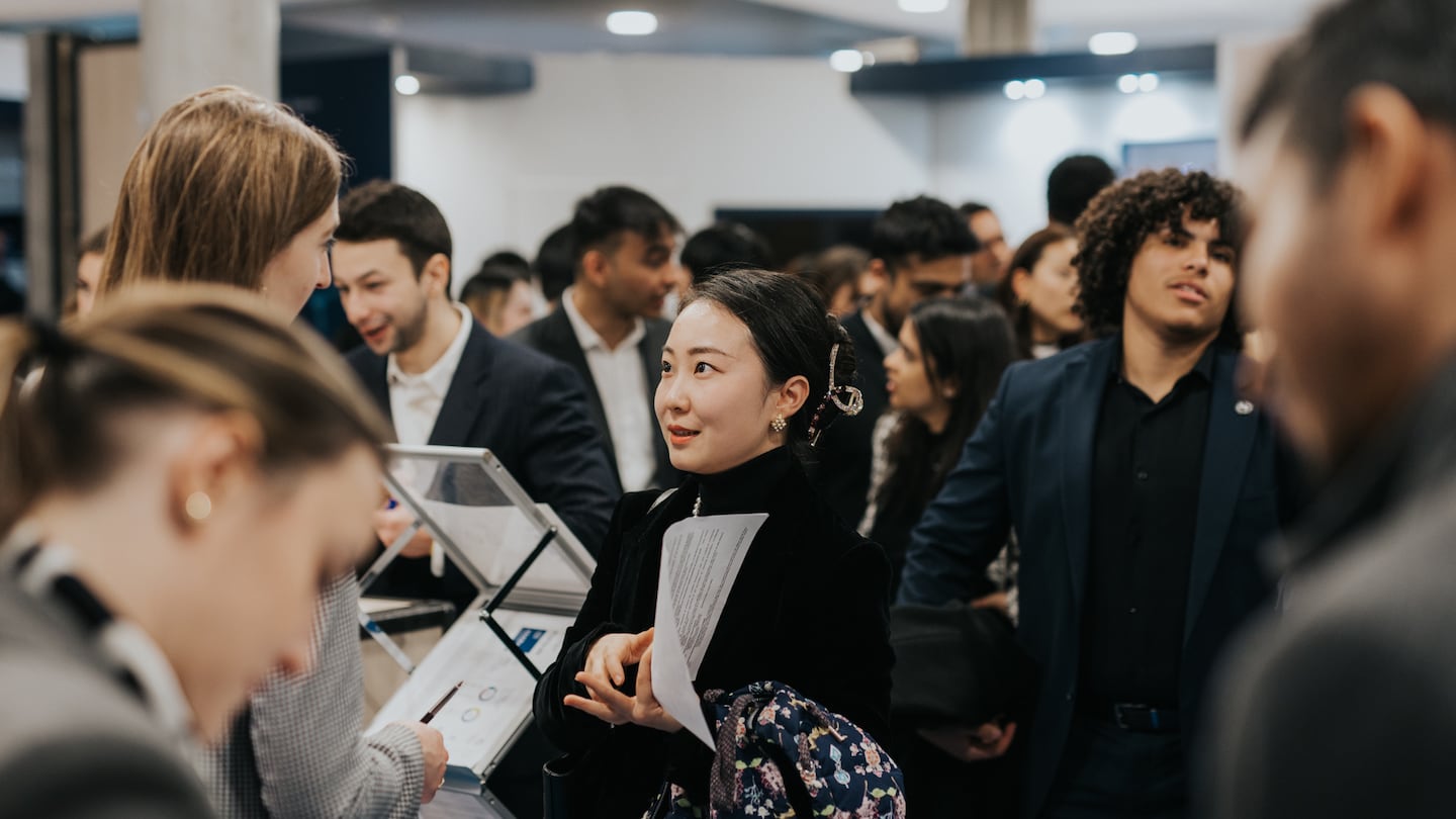 Students at a careers fair talk to industry professionals and take notes.