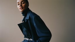 A woman in a blue coat looks into the camera